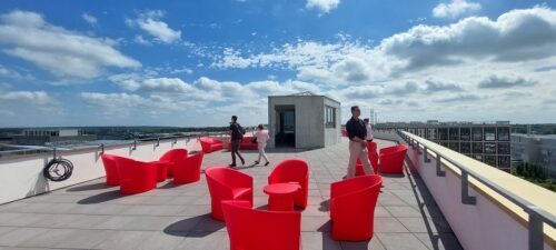 pessoas caminham no telhado de um prédio entre poltronas vermelhas