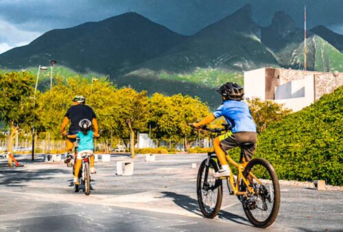 imagem mostra um homem e duas crianças andando de bicicleta em um espaço aberto