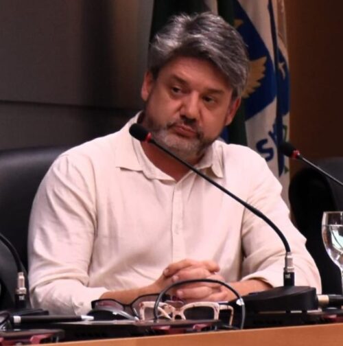 foto de um homem branco, com cabelo, barba e bigode grisalhos que está sentado e tem um microfone à frente