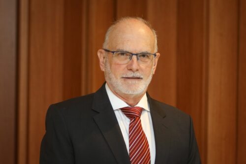 foto de um homem branco, com barba e bigode brancos e que está usando paletó preto e gravata vermelha